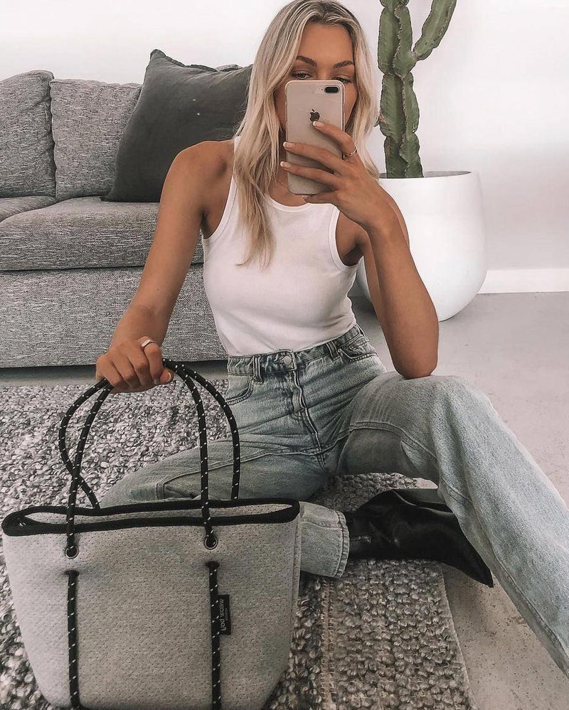 Blonde woman holding a light marle neoprene mini tote bag with black rope handles.