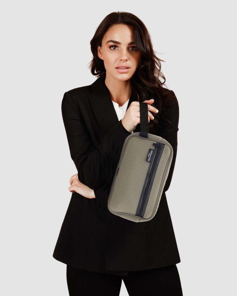 Woman holding a sage neoprene cosmetic bag with a front zip pocket and top handle.