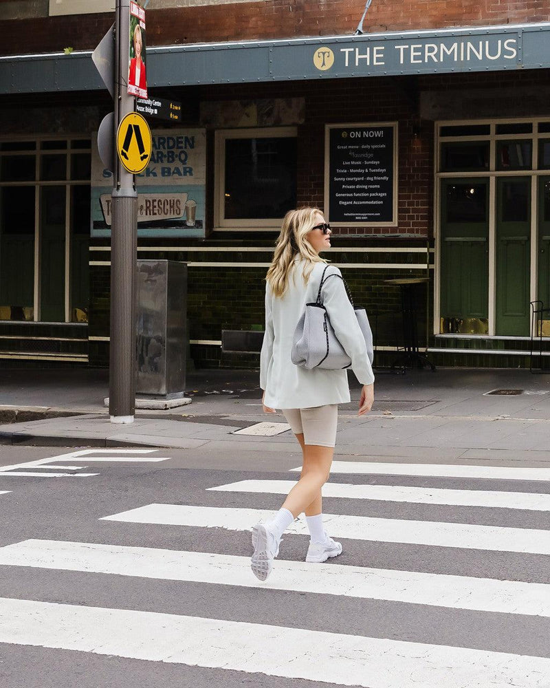 Woman in light marle Daydreamer neoprene tote bag with matching pouch, walking on a city street.