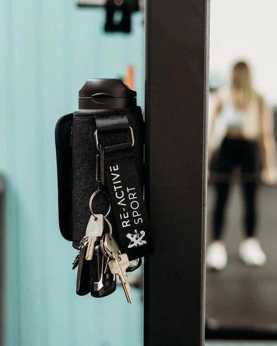 Black denim magnetic gym caddy holding a water bottle and keys, attached to gym equipment.