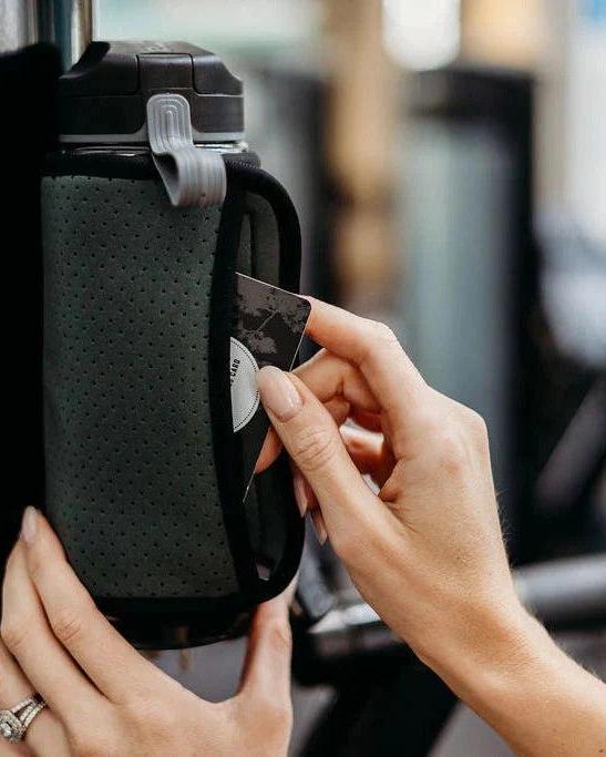 Petrol magnetic gym caddy holding a water bottle, with a hand inserting a card into its side pocket.