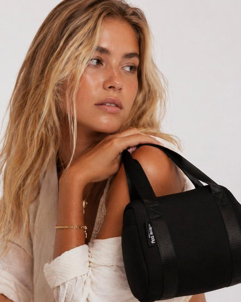 Blonde woman holding a black neoprene Vogue Mini Day Bag with a shoulder strap.